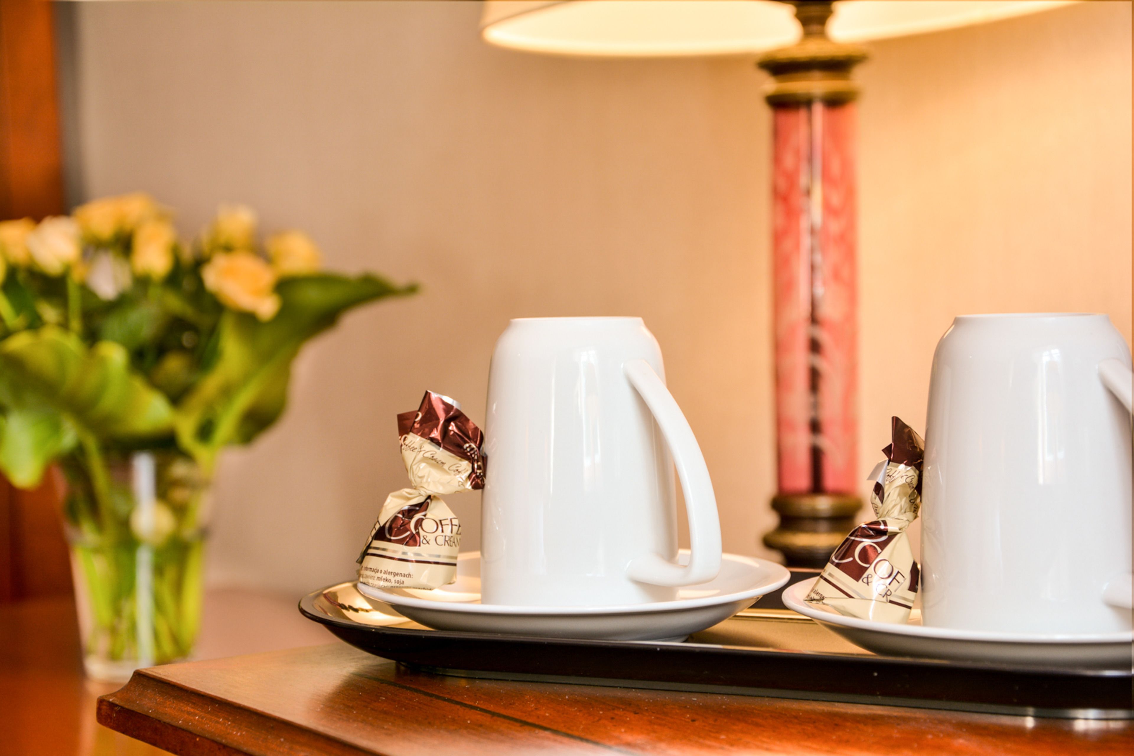 A table with two white coffee cups and saucers, a small figurine, and a vase with flowers.