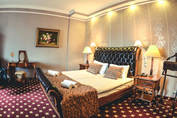 A hotel room with a large bed, two bedside tables with lamps, a wooden nightstand, a bench, and a mirror. - Komoda Club Residence (Kalisz)