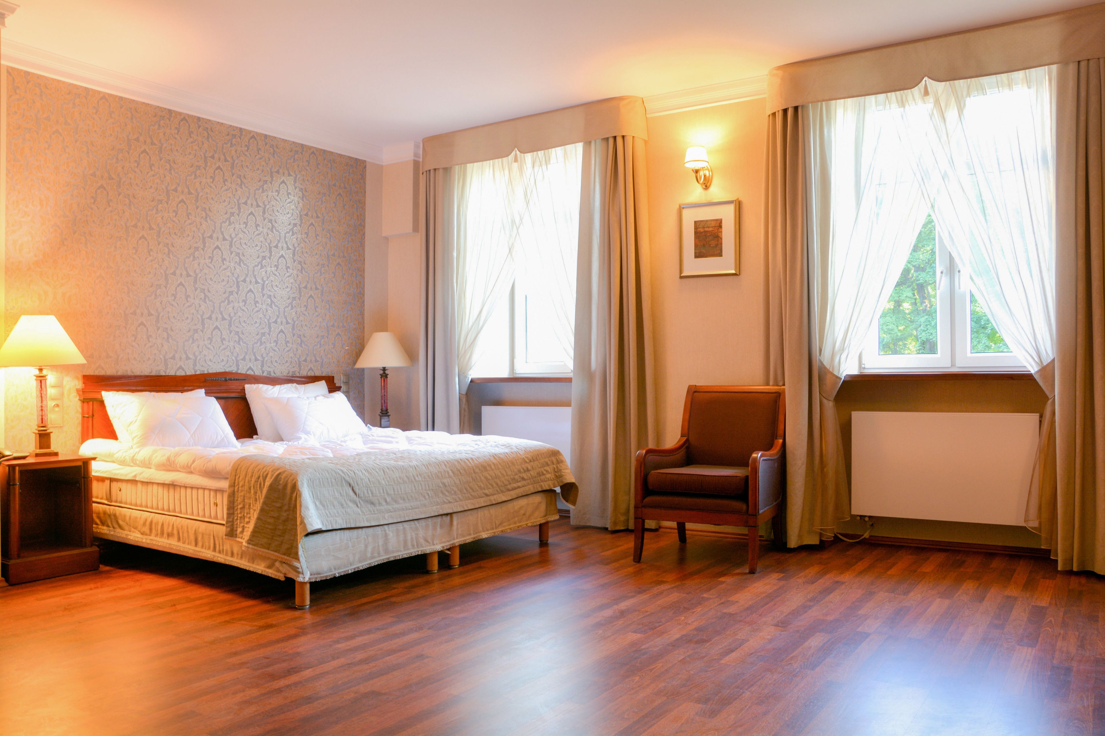 Een hotelkamer met een bed, twee bedlampen, een stoel en een raam met gordijnen.