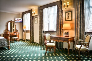 A hotel room with a bed, a desk, two chairs, a dresser, a mirror, a television, and a window with curtains. - Komoda Club Residence (Kalisz)