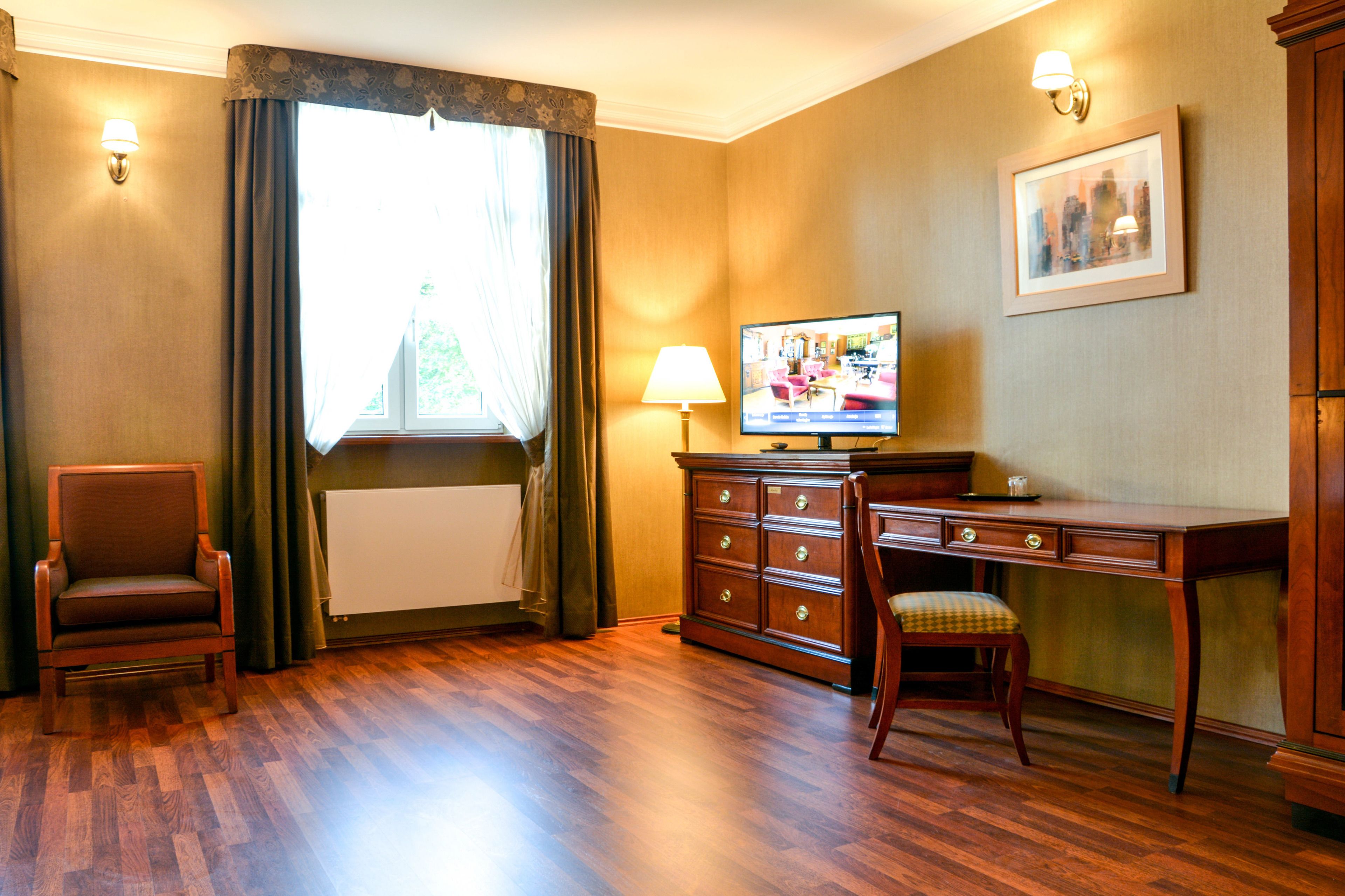 Une pièce avec un plancher en bois, un bureau avec une chaise, une télévision, une lampe et un tableau encadré au mur.