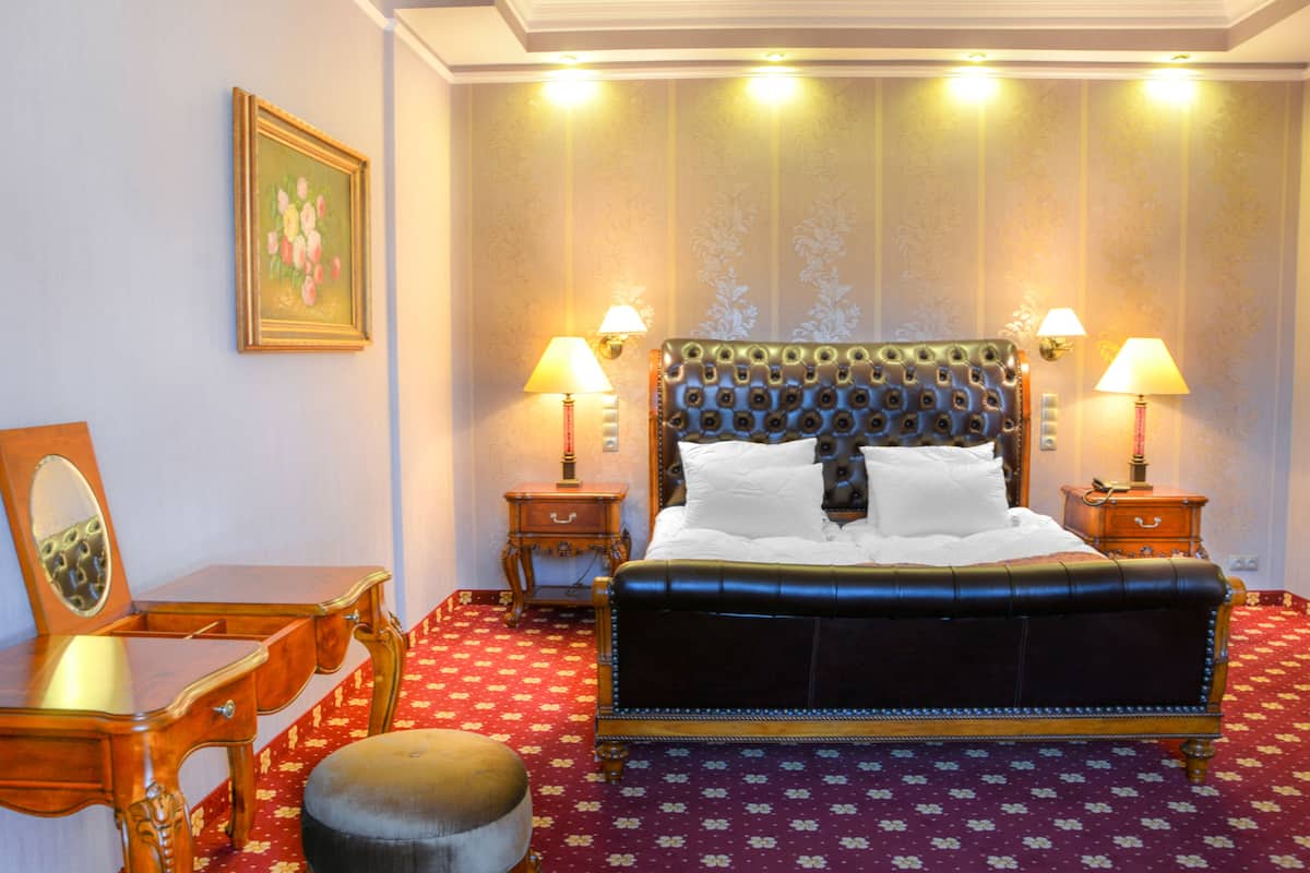 A hotel room with a large bed, two bedside tables with lamps, a wooden dresser, and a chair.