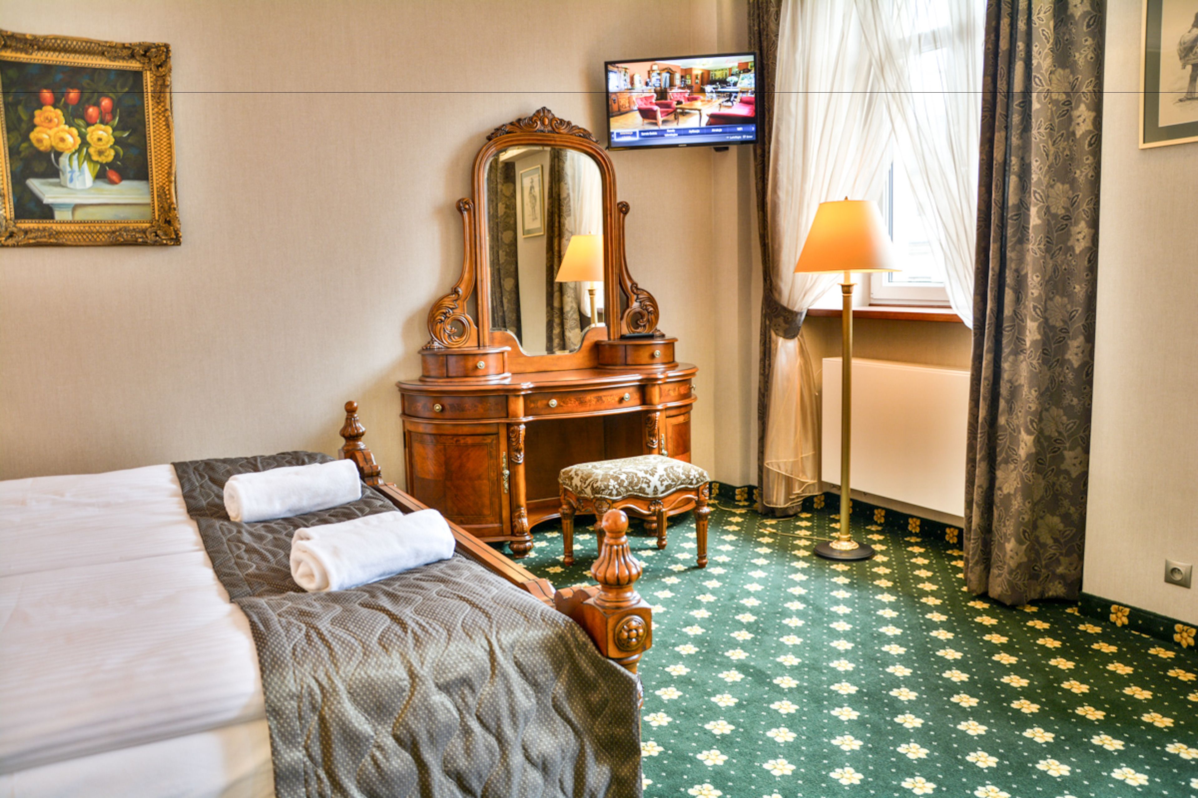 A hotel room with a bed, a wooden dresser, a mirror, a television, and a lamp.
