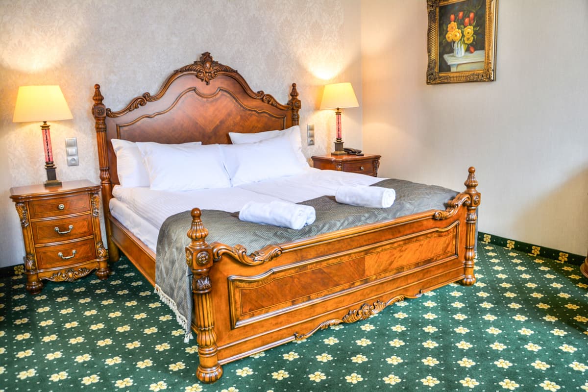 A wooden four-poster bed with white linens, two bedside tables with lamps, and a floral-patterned carpet.