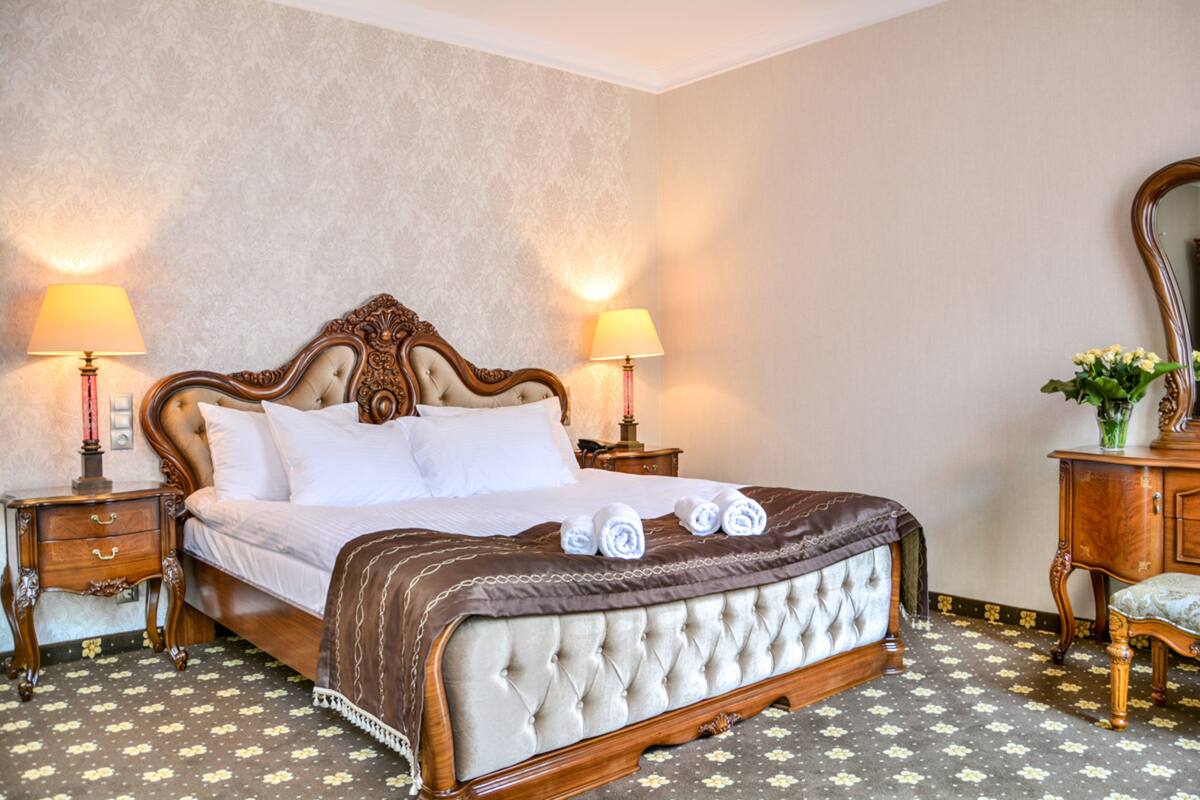 A large bed with a tufted headboard, two bedside tables with lamps, and a mirror on a dresser.