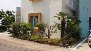 A building with a white exterior, a window with a wooden frame, and a sign with Korean text. - Living Stone Pension (Seogwipo)