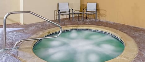 A hot tub with a metal ladder, surrounded by a beige floor and walls, with two chairs in the background.