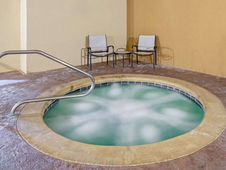 A hot tub with a metal ladder, surrounded by a beige floor and walls, with two chairs in the background.