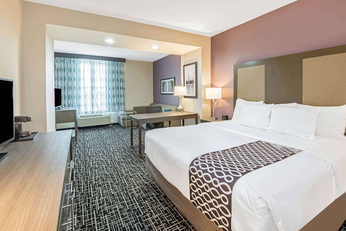 Una habitación de hotel con una cama grande, un escritorio, una silla, un televisor y una ventana con cortinas.