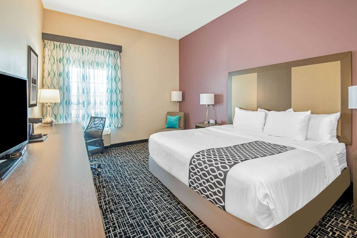 Habitación de hotel con una cama grande, un escritorio con televisión de pantalla plana, una silla y una ventana con cortinas estampadas.