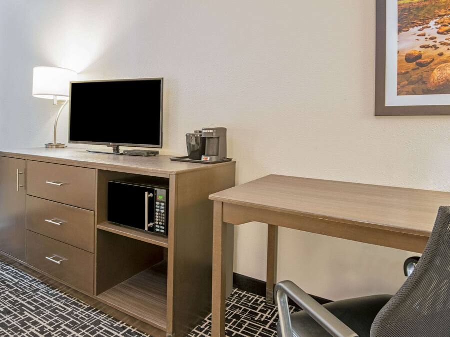 Una camera d'albergo con una scrivania, una televisione, una macchina del caffè e un quadro appeso al muro.