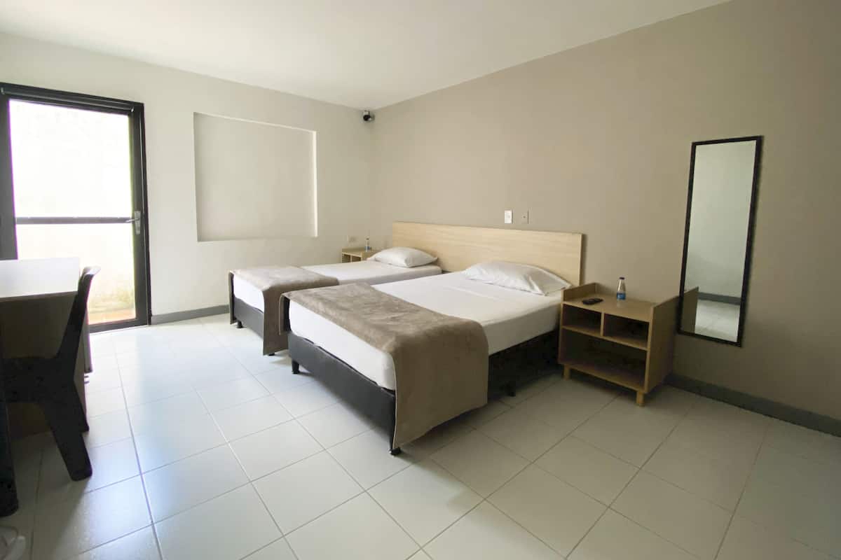 Ein Hotelzimmer mit zwei Betten, einem Schreibtisch, einem Stuhl, einem Spiegel und einem Fenster.