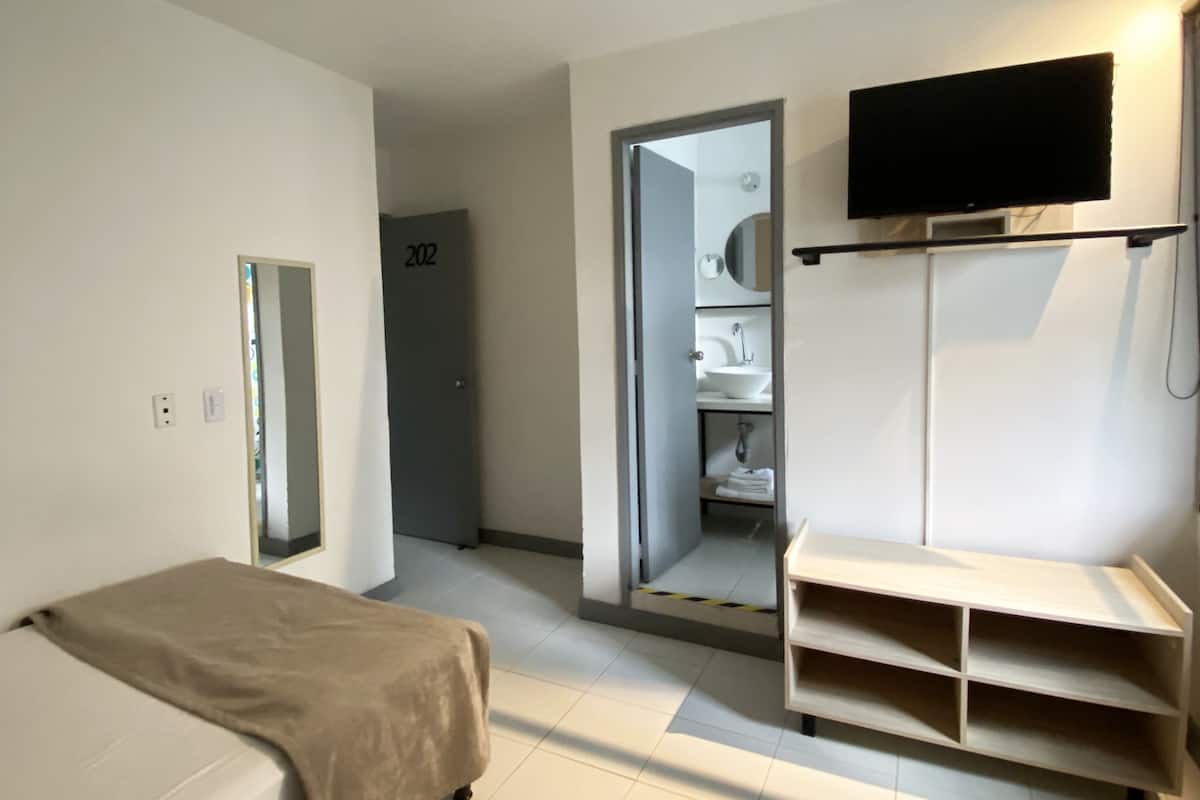 Ein Hotelzimmer mit einem Bett, einem an der Wand montierten Fernseher, einem Spiegel und einem Kleiderschrank.