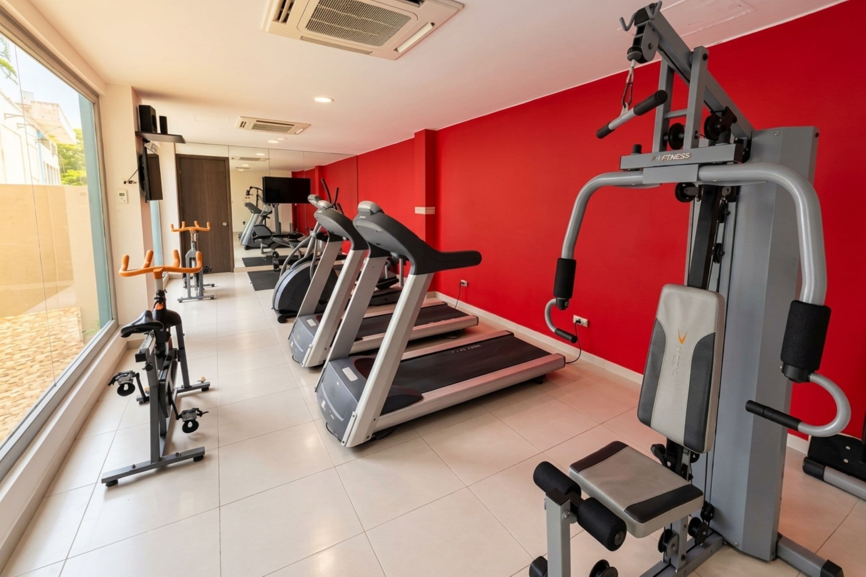 Un gimnasio con cintas de correr, máquinas de pesas y una pared roja.
