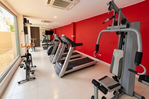 Un gimnasio con cintas de correr, máquinas de pesas y una pared roja.
