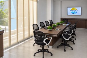 A conference room with a long table, black office chairs, potted plants, and a TV displaying a logo.