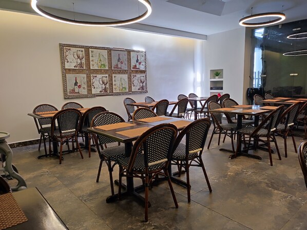 A restaurant interior with multiple tables and chairs, a wall with framed artwork, and a modern ceiling light fixture. - Hotel Portobelo Plaza las Ámericas (San Andrés)