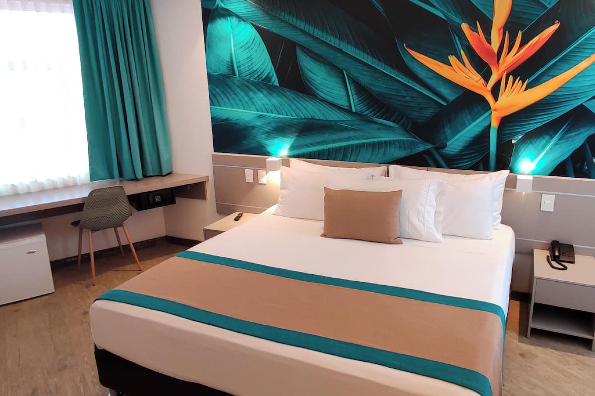 A hotel room with a bed, desk, chair, and a large tropical-themed wall mural.