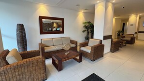 A lobby with wicker furniture, a coffee table, and a mirror on the wall. - Hotel Portobelo Plaza las Ámericas (San Andrés)