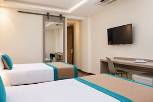 A hotel room with two beds, a desk, a chair, a television, and a sliding door.