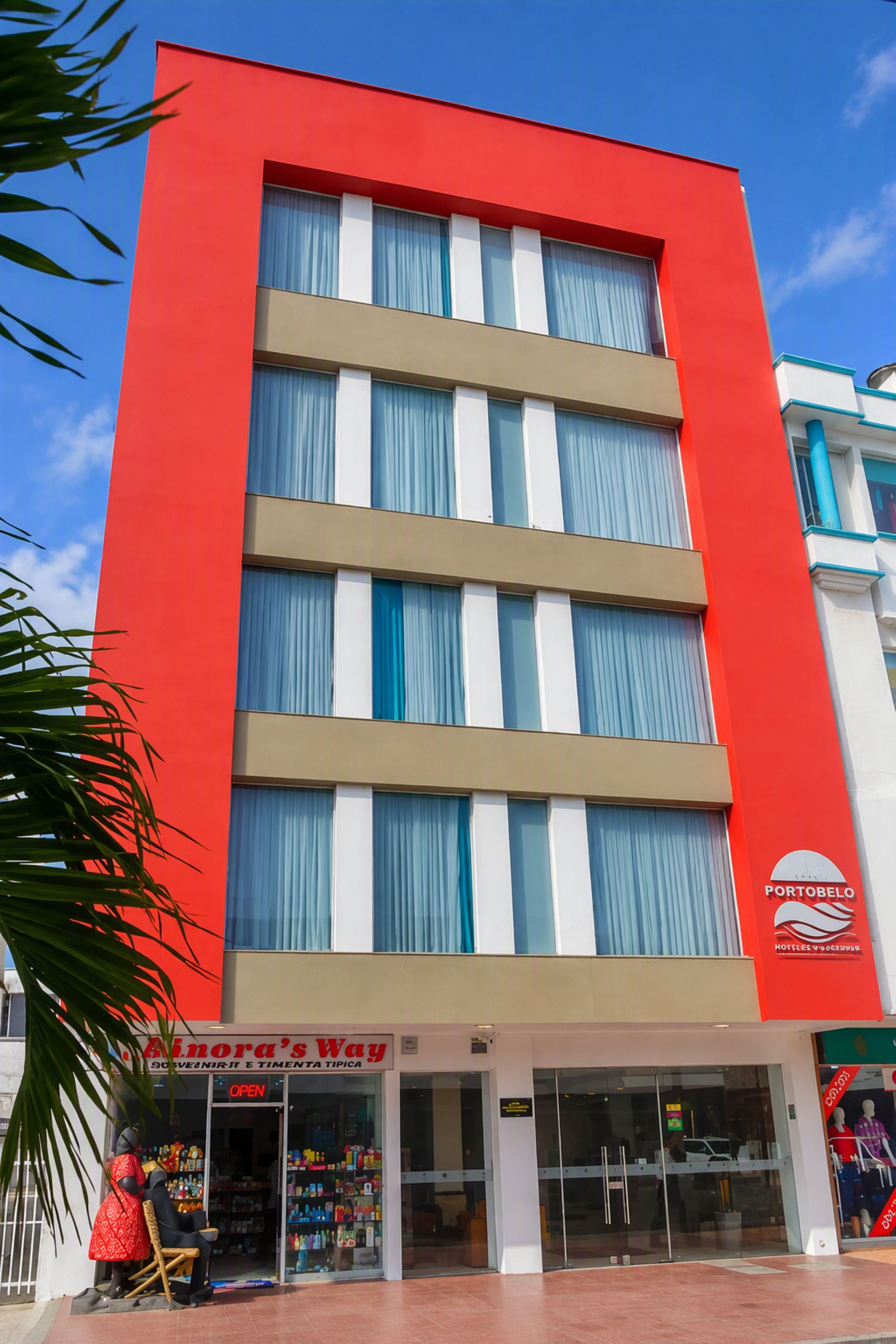 Un edificio de varios pisos con fachada roja, una tienda a nivel de calle llamada 'Ainora's Way', y un letrero de hotel visible que dice 'PORTOBELLO'.