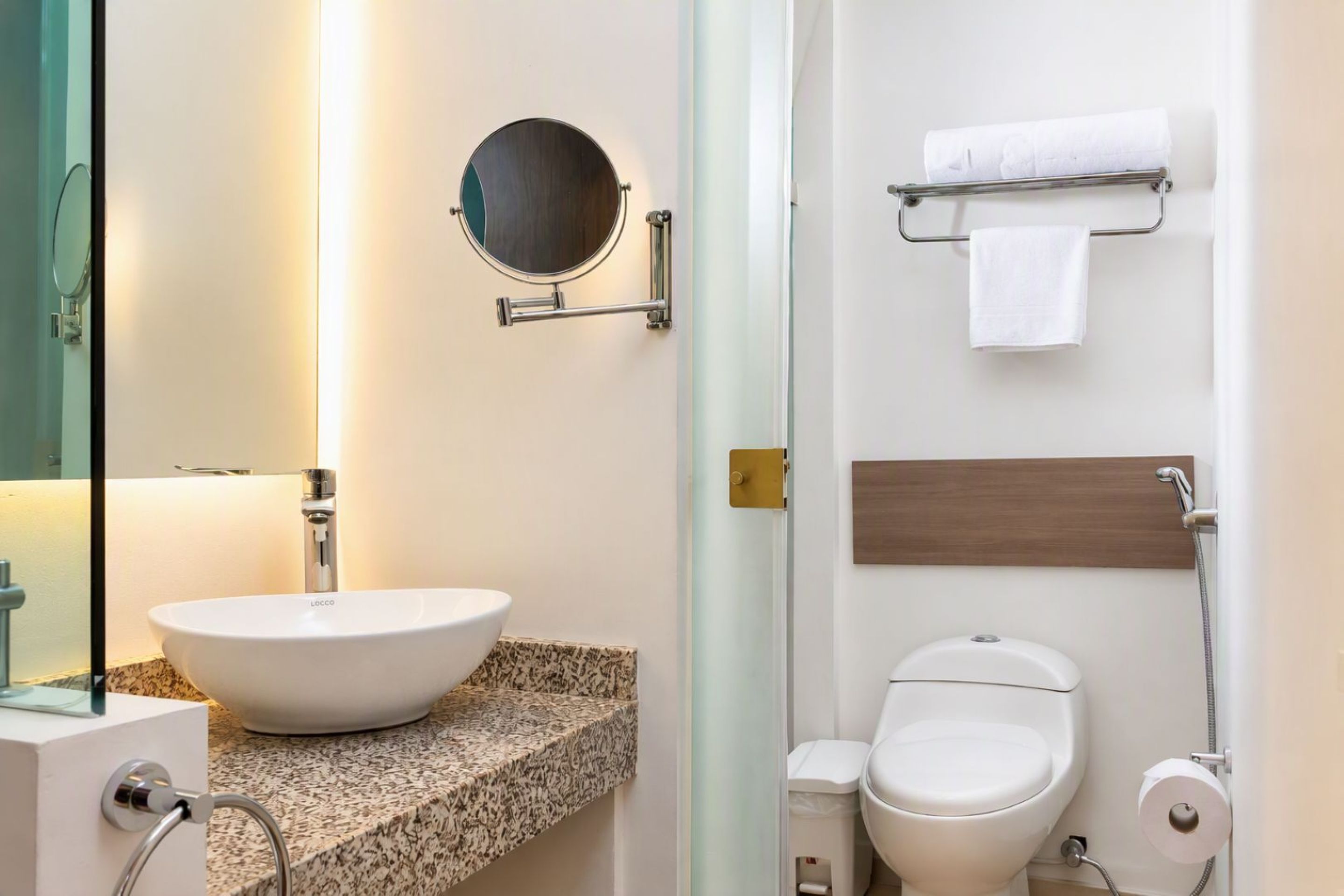 Un baño con un espejo redondo, un lavabo, un inodoro y un perchero para toallas.
