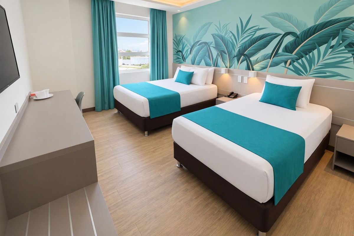 Una habitación de hotel con dos camas, un escritorio y un ventanal con cortinas.