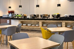 Una cafetería moderna con mostrador, zona de estar y diversas opciones de comida y bebida.