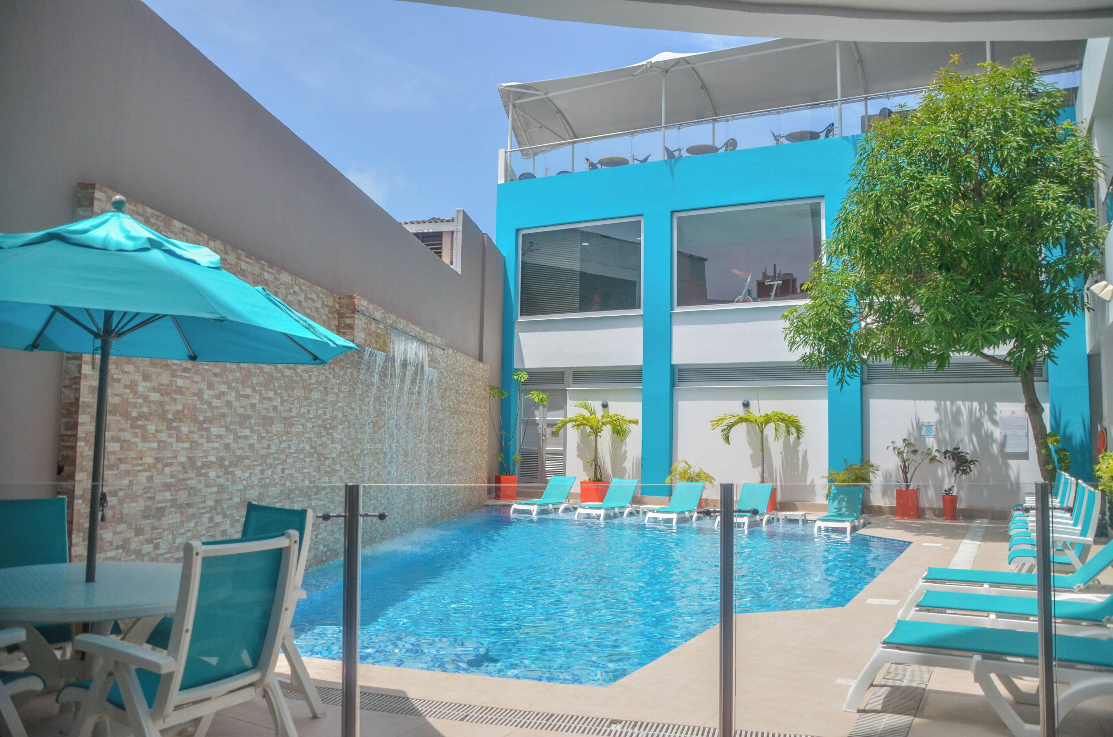 A swimming pool area with lounge chairs and umbrellas, a stone wall, and a modern building with large windows.