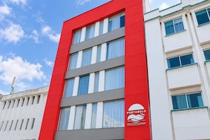 Ein modernes Gebäude mit roter Fassade und zahlreichen Fenstern, mit dem Logo von Portobelo Hotels & Resorts.