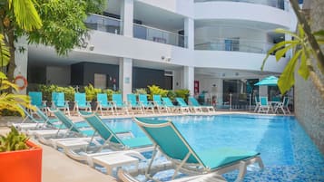 Una piscina al aire libre, sombrillas, sillones reclinables de piscina