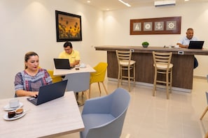 Habitación de hotel moderna con comedor, bar y recepción. Tres personas sentadas en mesas con portátiles.