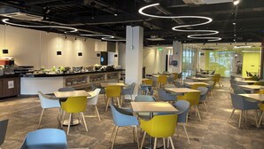 A modern cafe with round tables and chairs, a counter with food and drink options, and a bright, circular ceiling light fixture. - Hotel Portobelo Plaza las Ámericas (San Andrés)