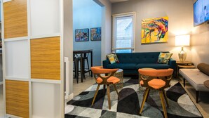 A modern living room with a teal sofa, orange chairs, a patterned rug, and artwork on the walls. - The Urban San Francisco (San Francisco)