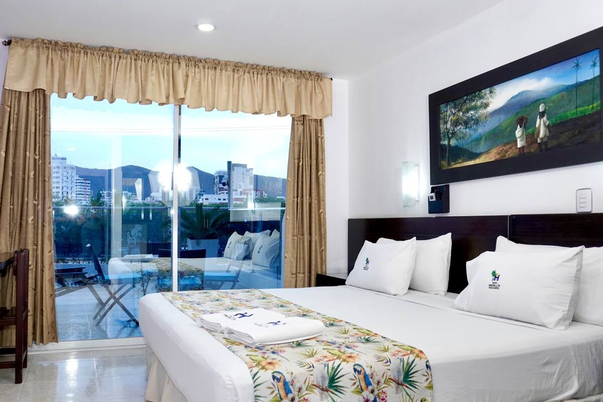 Una habitación de hotel con una cama grande, un balcón con vista a la ciudad y un cuadro en la pared.