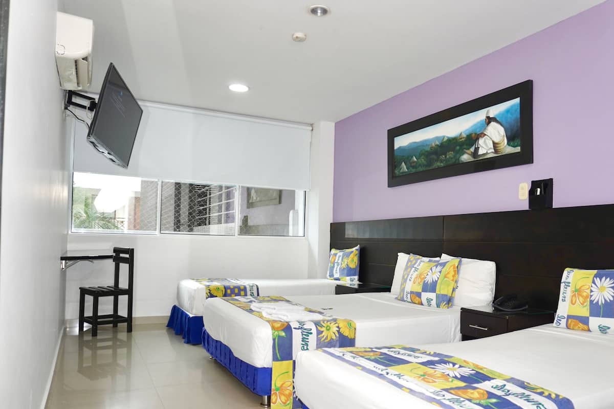 Habitación de hotel con dos camas, un escritorio, una silla, un televisor montado en la pared y una ventana con vistas a edificios.
