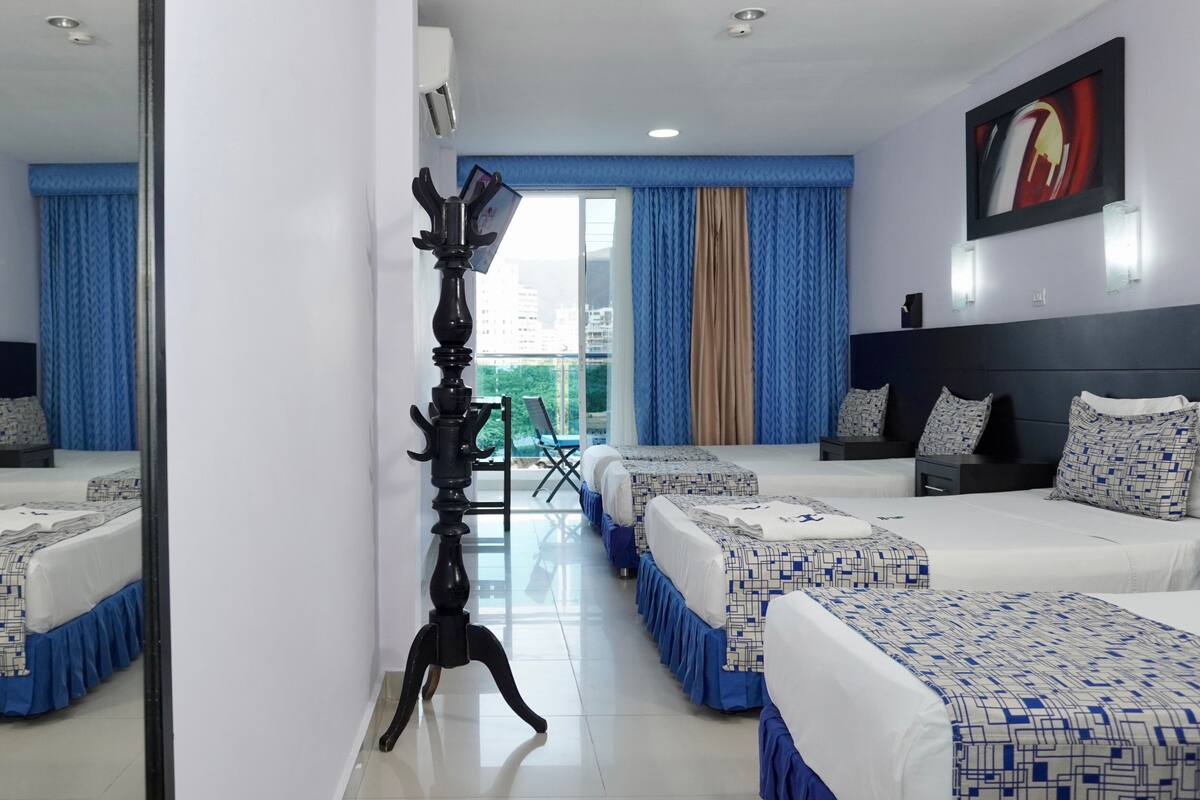 Habitación de hotel con dos camas, un espejo grande, una lámpara de pie y vistas a la ciudad a través de la ventana.