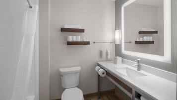 Une salle de bain moderne équipée de toilettes, d’un lavabo et d’une douche. On y trouve des étagères en bois où sont rangées des serviettes et des articles de toilette.