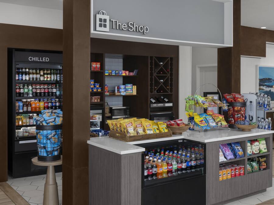Uma loja com área de bebidas geladas, expositores de lanches e diversos produtos embalados.