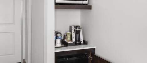 A kitchenette with a microwave, coffee maker, and storage cabinets.