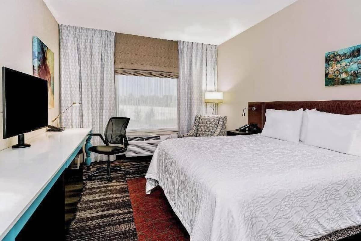 A hotel room with a bed, desk, chair, TV, and curtains.