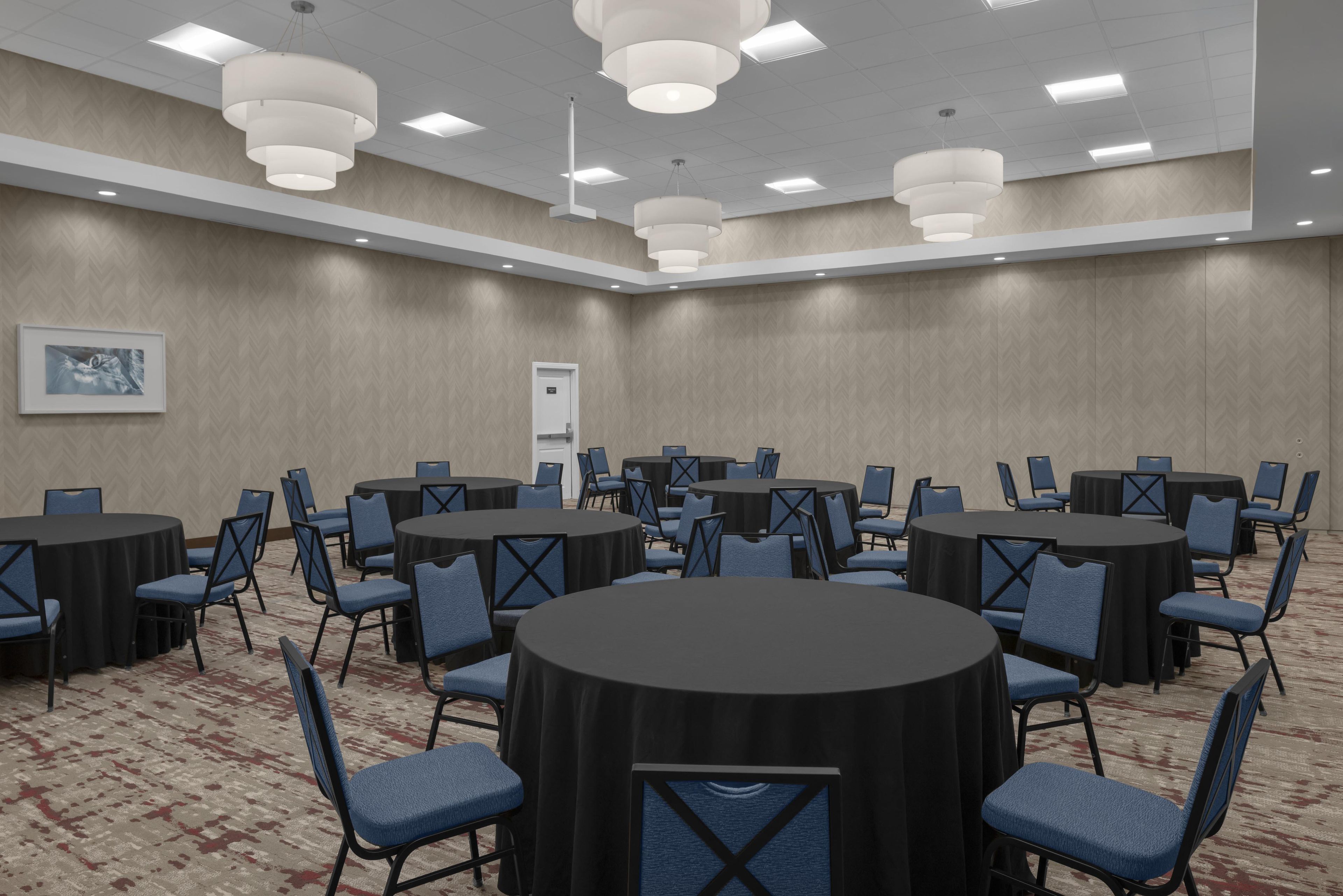 A conference room with round tables and chairs, a patterned carpet, and a framed picture on the wall.