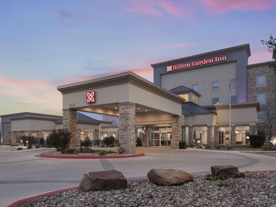 Ein Hilton Garden Inn mit modernem architektonischen Design, das einen markanten Eingang, Steinsäulen und einen gepflegten Außenbereich mit Steinen und Bepflanzung zeigt.