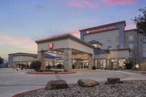 A Hilton Garden Inn with a modern architectural design, featuring a prominent entrance, stone pillars, and a well-maintained outdoor area with rocks and landscaping. - Hilton Garden Inn San Marcos (San Marcos)