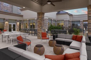 An outdoor patio area with seating arrangements, stone pillars, and a view of the building's exterior. - Hilton Garden Inn San Marcos (San Marcos)