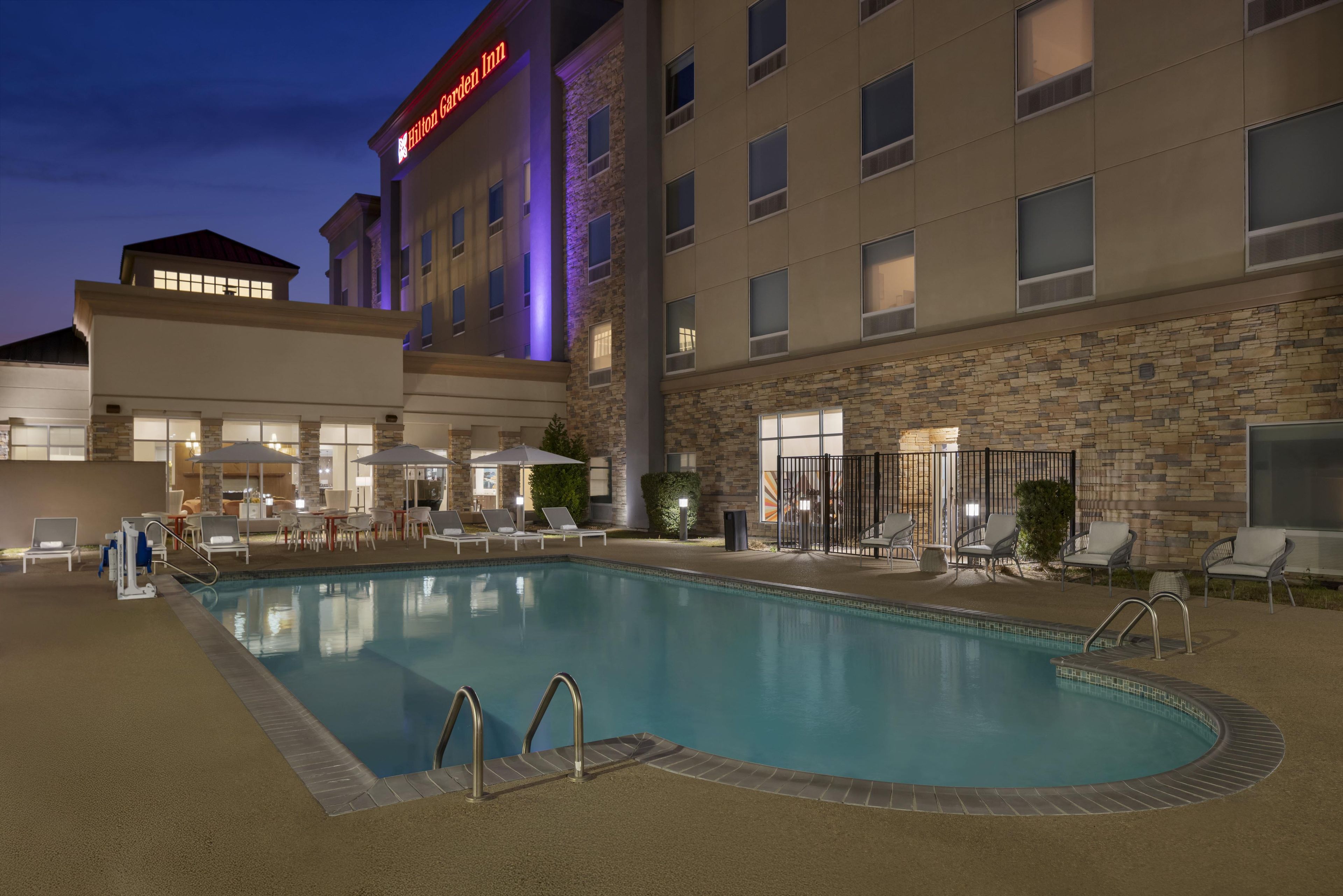 A hotel with a swimming pool, lounge chairs, and a stone facade.