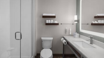 Un baño moderno con cabina de ducha de vidrio, inodoro, lavamanos con espejo y toalleros.
