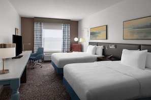 A hotel room with two beds, a desk with a computer, a chair, a window with curtains, a painting on the wall, and a bedside table with a lamp. - Hilton Garden Inn San Marcos (San Marcos)