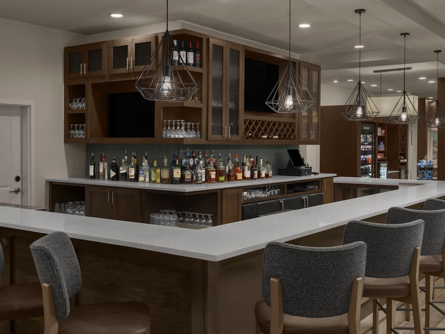 A bar area with a long counter, multiple seating options, and a variety of bottles and glasses.