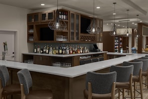 A bar area with a long counter, multiple seating options, and a variety of bottles and glasses. - Hilton Garden Inn San Marcos (San Marcos)